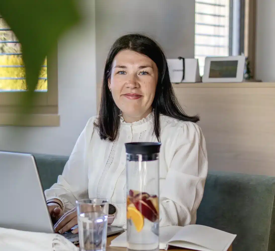 Ella Neff sitzt lächelnd mit ihrem Laptop an einem Tisch