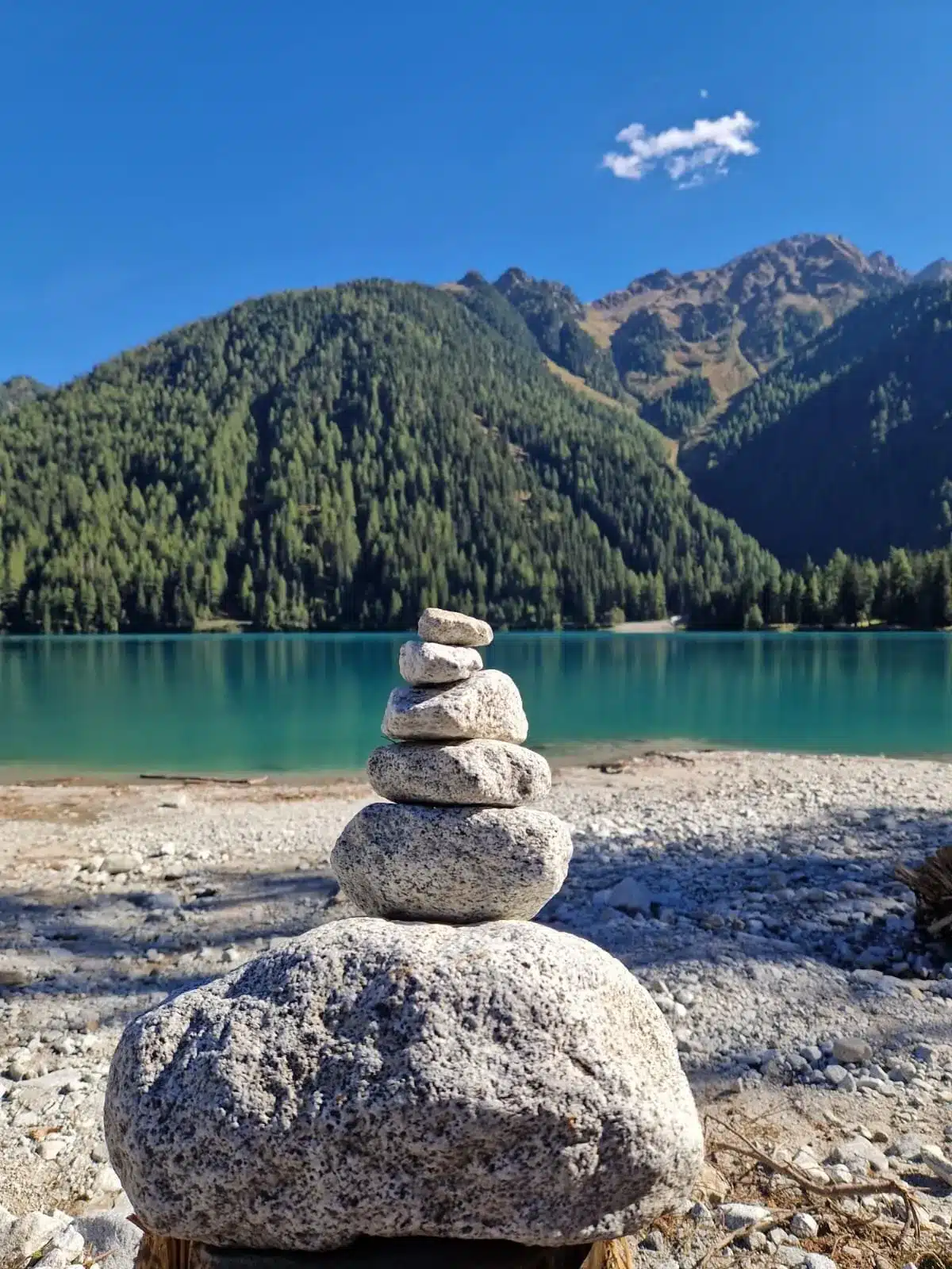 Gestapelte Steine an einem türkisfarbenen Bergsee vor einem Nadelwald